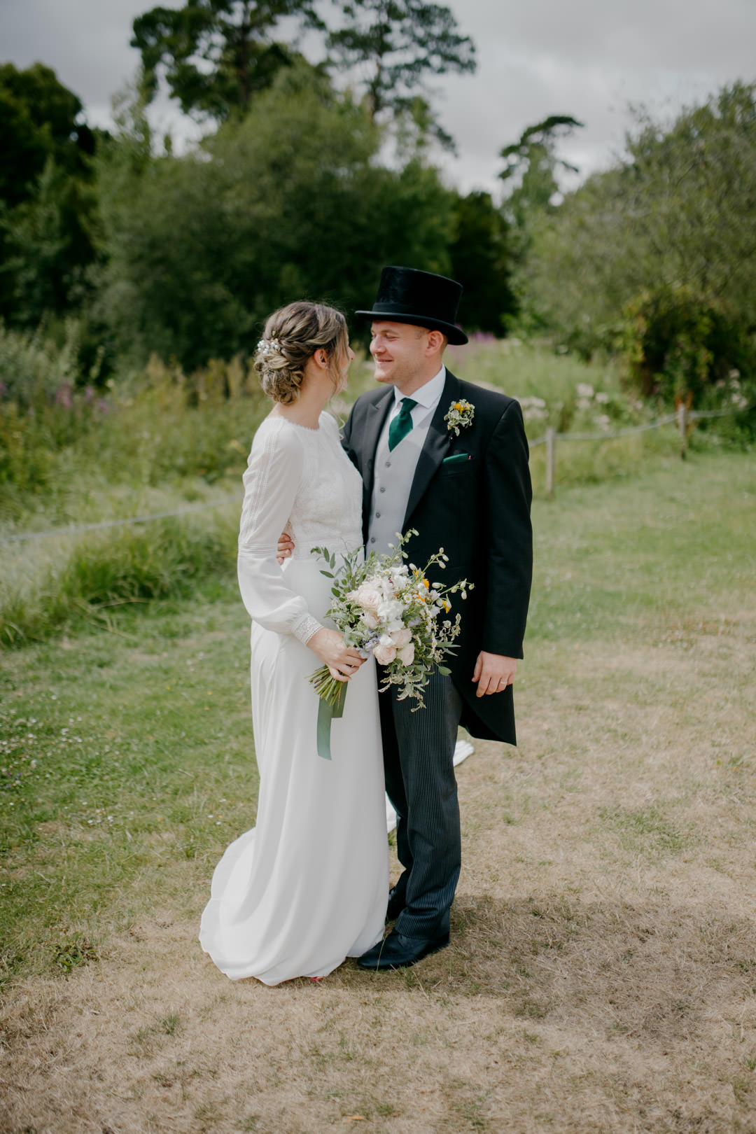 bride and groom stood in green field holding flowers
