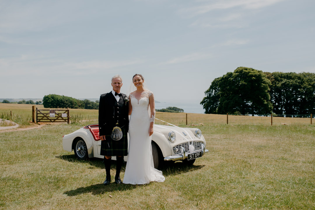 wedding bride stood next to white sports car in meadow during day time